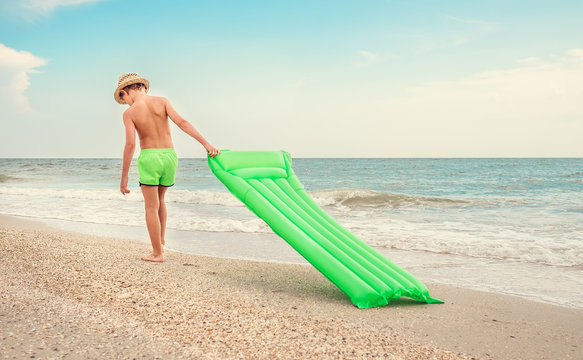 Boy with swimming mattress walks on sand sea beach