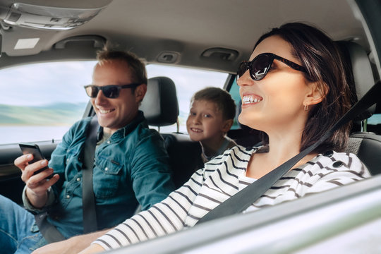 Happy family auto traveling concept image. Car interior view of female driving, man dealing mobile phone and little son smiling into camera