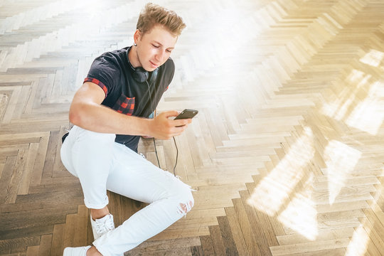 Young man using his smartphone with headphones, listen the music and sit on the floor .