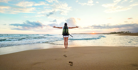 Woman backpacker greeting a sunset at the ocean coast