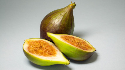Green figs, one fruit cut in two halves and zhadi is a whole fruit on a light gray background, close-up