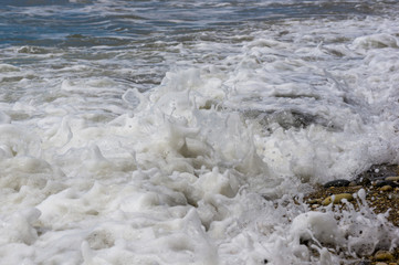 pebble stones on the sea beach, the rolling waves of the sea with foam