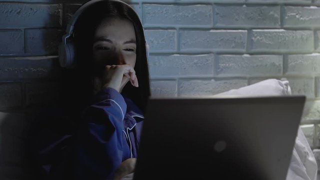 Crying girl in headphones watching melodramatic movie on laptop at night
