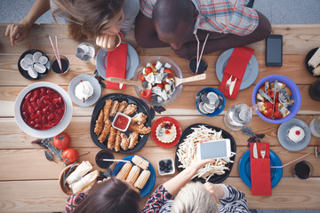 Top view of group of people having dinner together while sitting at wooden table. Food on the table. People eat fast food.