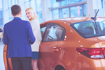 Dealer with woman stands near a new car in the showroom
