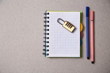 No idea or inspiration concept: lock lying on a notebook and colored pens on a gray background.