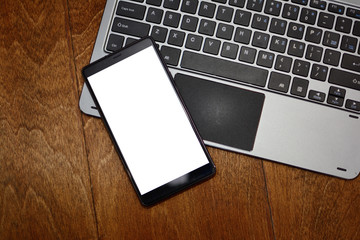 The smartphone and the keyboard of the laptop on a wooden background. Top view