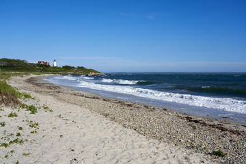 sandy beach and waves with Nobska Light lighthouse in the distance