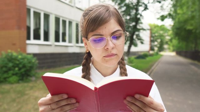 Serious  young girl in glasses reading book and surprised, near school, university, motivated student with big dreams studying abroad, creative happy manager starts successful career. Schoolgirl 