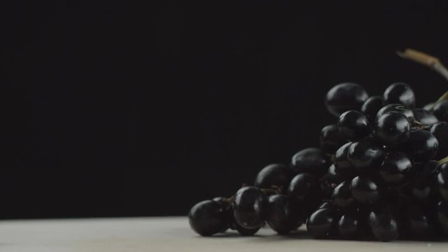 in the video we see a bunch of grapes, two grapes rolling on the table from the bunch, black background