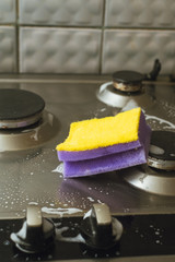 Violet - yellow sponge with a metal gas stove. Cleaning the dirt with a sponge with foam.