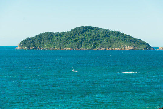 Vista do alto de um rochedo para o mar e uma ilha deserta florestada ao horizonte.