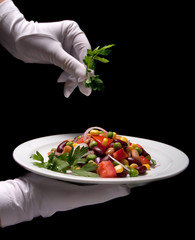 Healthy bean and corn salad on a white plate served by someone in white gloves