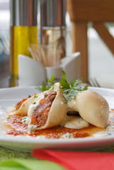 Pasta shell conchiglioni with minced meat filling in sauce close-up in dish.