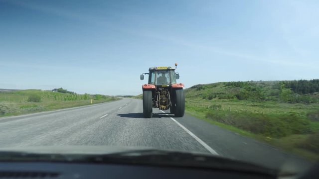 In a car following an old tractor driving on a road, Then driving past it.Two other cars in shot also driving. Driving in green nature.