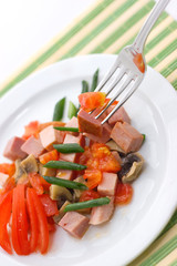 Delicious salad of ham, tomato, pepper and green onion on a white plate.
