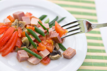 Delicious salad of ham, tomato, pepper and green onion on a white plate.