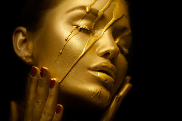 Sexy beauty woman with golden metallic skin. Gold paint smudges drips from the face and sexy lips....