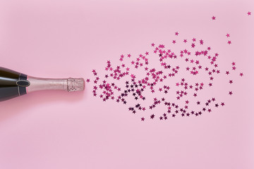 Pink Champagne bottle with pink confetti stars on light pink background. Copy space, top view.