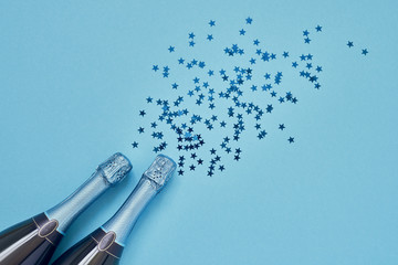 Two Blue Champagne bottle with blue confetti stars on light blue background. Copy space, top view.