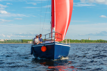 sailboat with red sails on the background of the shore with an urban landscape