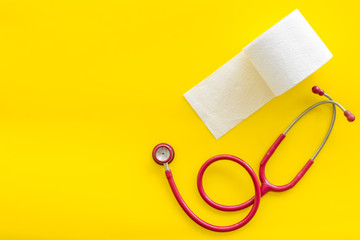 Proctology concept with toilet paper roll and stethoscope on yellow background top view space for text