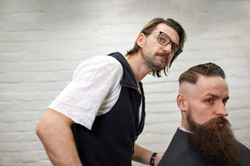 Brutal guy in modern Barber Shop. Hairdresser makes hairstyle a man with a long beard. Master hairdresser does hairstyle by scissors and comb