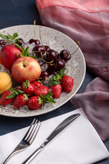 Healthy fruit platter, strawberries, apples, peaches, apricots on a dark gray wooden table, top view, close-up, selective focus.