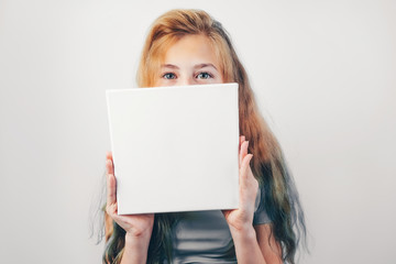 Beautiful caucasian girl with mockup poster, grey wall on background. Girl holding in her hands...