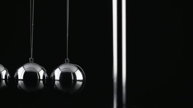 The chrome balls of a Newton&rsquo;s Cradle colliding in slow motion