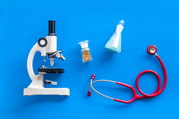 Medical tests on work table of doctor with microscope, stethoscope, test tube, pills on blue background top view