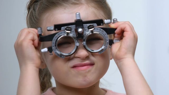 Female child squinting eyes wearing optical trial frame, eye examination, myopia
