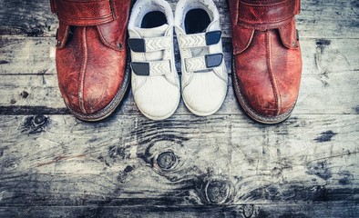 Father boots and baby shoes on wooden background, fathers day. Daddy's boots and baby's shoes, fathers day concept.