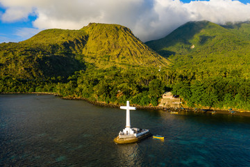 Aerial drone view of a cross in the ocean with steep Mount Vulcan and Mount Hibok-Hibok behind...