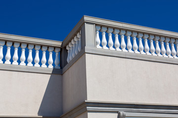 the corner of the end of the building baroque architecture details of stone railings with white balustrades close up against a blue sky.