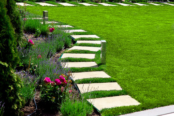 back yard with a marble stone walkway of square tiles near a green meadow with a flower bed, garden...