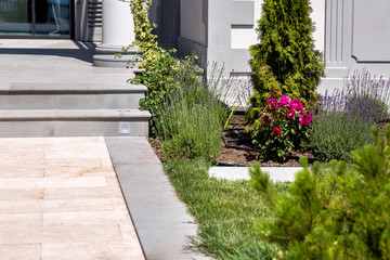 marble walkway with flowerbed at the entrance to the house with stone steps on a sunny summer day, details of the backyard with landscape design and architecture of the house.