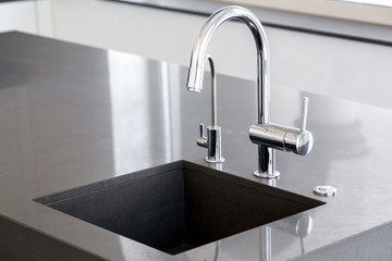 kitchen sink of dark gray stone with chrome faucet in a clean kitchen with a glossy work surface,...