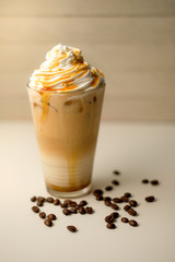 Ice coffee in the glass topped whipping cream with coffee beans. Cold summer drink on wooden background and copy space. Advertising for caramel mocha and chocolate beverage for the cafe.