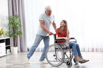 Happy grandfather and teenage girl in wheelchair at home