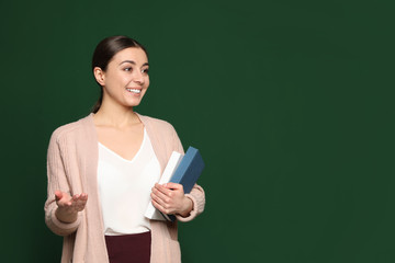 Portrait of young teacher with books on green background. Space for text
