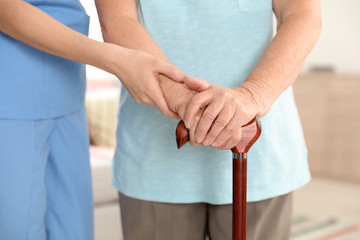 Nurse assisting elderly woman with cane indoors, closeup