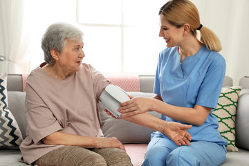 Nurse measuring blood pressure of elderly woman indoors. Assisting senior people