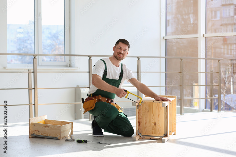 Wall mural Carpenter in uniform making furniture indoors. Professional construction tools