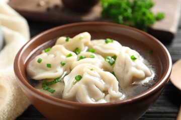 Bowl of tasty dumplings in broth on table, closeup