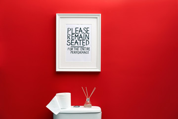 Toilet bowl and funny sign near red wall. Bathroom interior