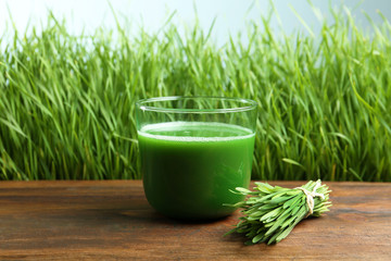 Glass of juice on wooden table near fresh wheat grass