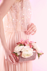 Woman holding elegant handbag with spring flowers on pink background, closeup