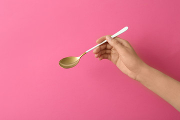 Woman holding empty table spoon on color background, closeup