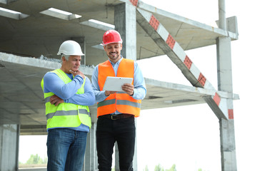 Professional engineer with tablet and foreman in safety equipment at construction site. Space for...